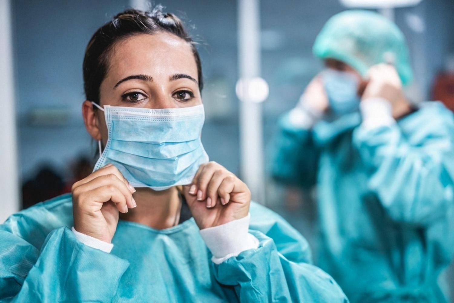 Female dental surgeon in scrubs preparing for a procedure with a colleague behind her
